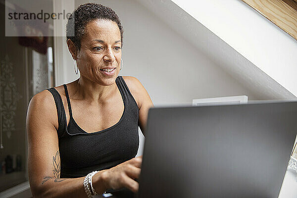 Reife Frau im Tanktop  die von zu Hause aus am Laptop arbeitet