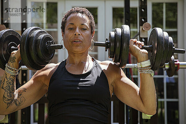 Starke reife Frau beim Gewichtheben im sonnigen Hinterhof