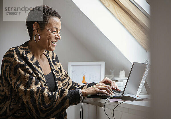 Lächelnde reife Frau  die von zu Hause aus am Laptop arbeitet
