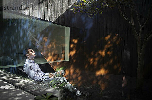 Ruhiger Mann sitzt im Sonnenlicht im Innenhof