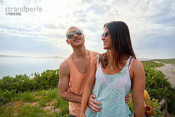 Glückliches Paar mit Sonnenbrille und Tanktops am Meeresstrand