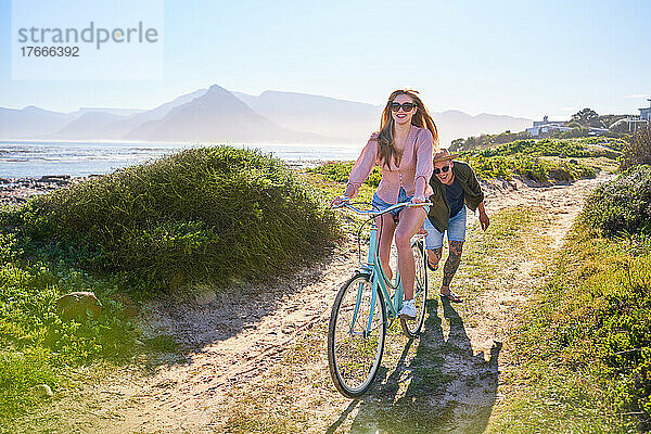 Unbekümmertes Paar fährt Fahrrad auf sonnigem Sommerstrandweg