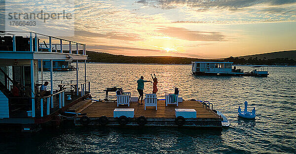 Unbeschwertes Paar tanzt bei Sonnenuntergang auf der Terrasse des Hausboots am See