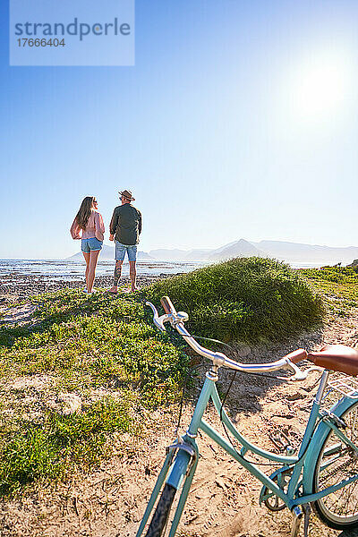 Paar genießt sonnigen Sommerblick auf das Meer vom Strand aus hinter dem Fahrrad