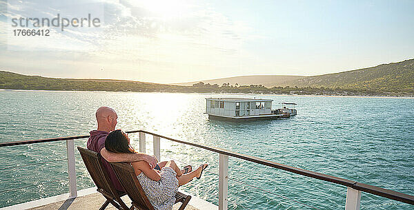 Unbeschwertes Paar entspannt sich auf der Terrasse des Hausboots am sonnigen Sommersee