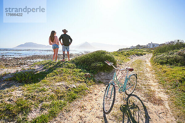 Paar steht mit dem Fahrrad am sonnigen  sommerlichen Sandstrand am Meer