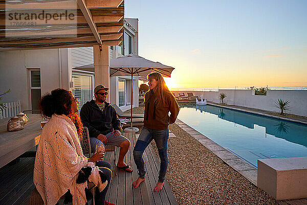 Freunde unterhalten sich bei Sonnenuntergang auf der sonnigen Terrasse am Pool