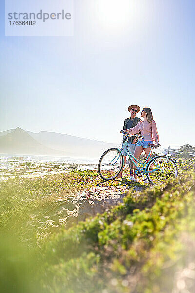Glückliches Paar mit Fahrrad am sonnigen Sommerstrand