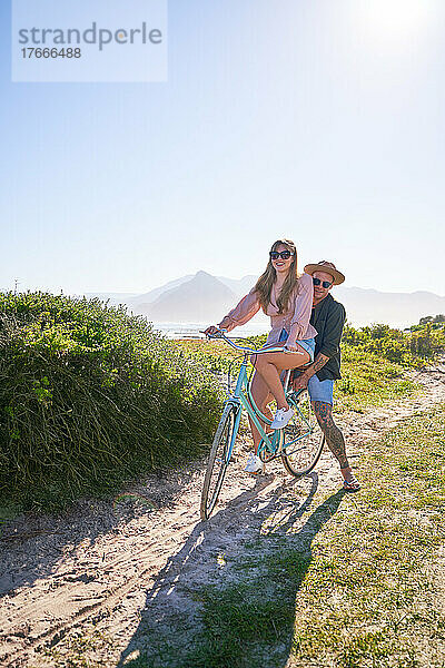Glückliches Paar fährt Fahrrad auf sandigem Sommerstrandweg