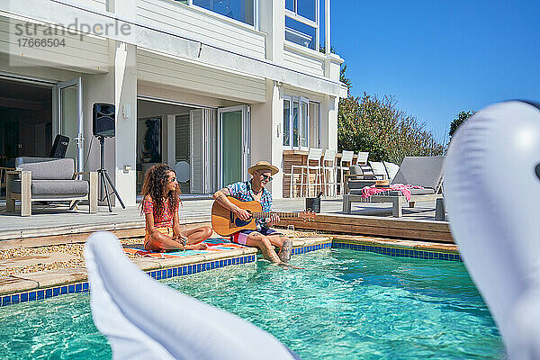 Paar entspannt sich und spielt Gitarre am sonnigen Luxushaus-Swimmingpool