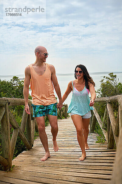 Glückliches Paar hält Händchen und geht auf der Strandpromenade spazieren