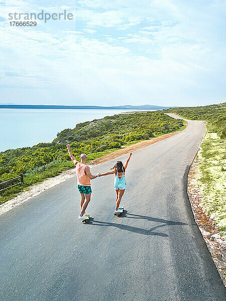 Unbekümmertes Paar fährt Skateboards auf sonniger Meeresstraße