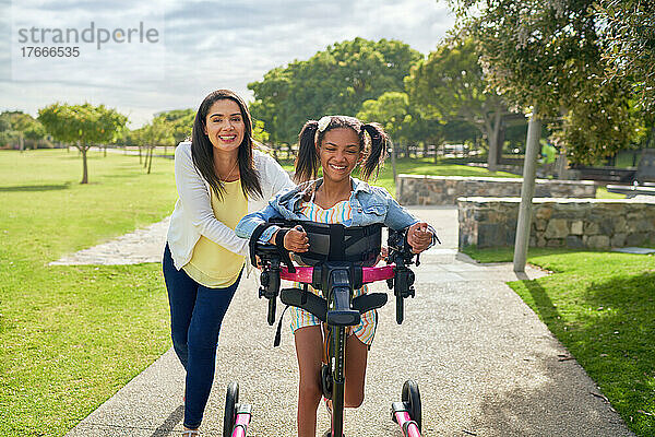 Glückliche Mutter und behinderte Tochter gehen mit Rollator im sonnigen Park