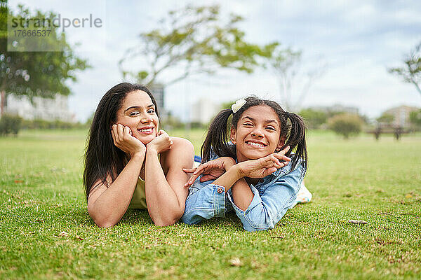 Porträt einer glücklichen brünetten Mutter und Tochter  die im Parkgras liegen