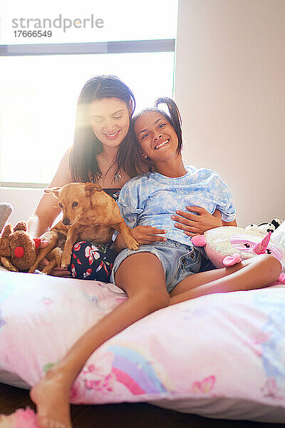 Porträt einer glücklichen behinderten Tochter mit Mutter und Hund auf dem Bett