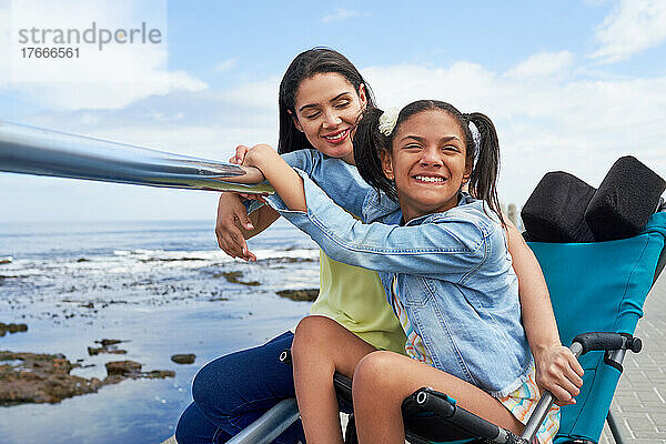Porträt glückliche Mutter und behinderte Tochter im Kinderwagen am Strand
