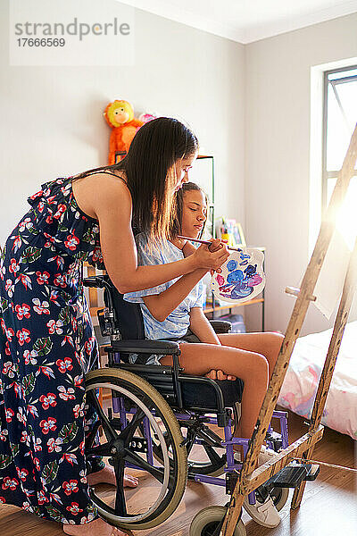 Mutter und behinderte Tochter im Rollstuhl malen zu Hause