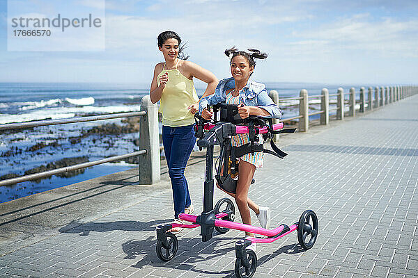 Mutter und behinderte Tochter joggen mit Rollator auf der Strandpromenade