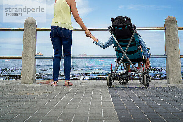 Mutter hält Händchen mit behinderter Tochter im Kinderwagen am Strand