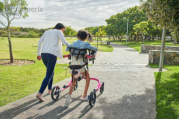 Mutter und behinderte Tochter gehen mit Rollator im sonnigen Park spazieren