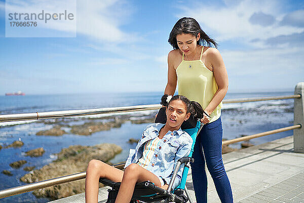 Mutter schiebt behinderte Tochter im Kinderwagen auf der Meerespromenade