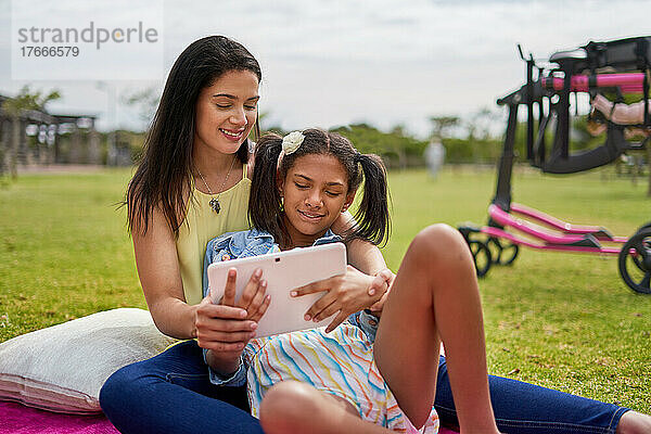 Mutter und behinderte Tochter nutzen digitales Tablet auf Decke im Park