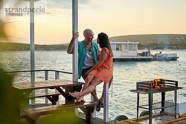 Glückliches Paar entspannt und unterhält sich auf der Terrasse des Hausboots am See