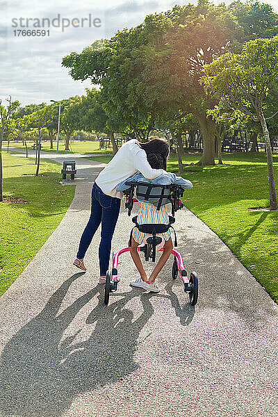 Zärtliche Mutter umarmt Tochter im Rollator im sonnigen Park