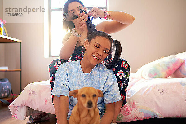 Mutter repariert Haare für Tochter mit Hund im Schlafzimmer