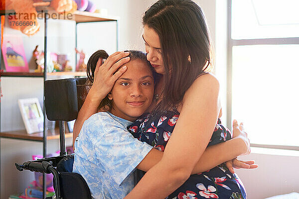 Porträt einer liebevollen Mutter  die ihre behinderte Tochter zu Hause umarmt
