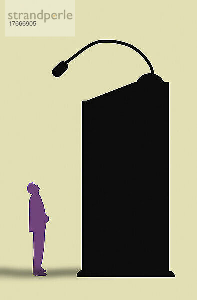 Kleiner Mann blickt von einem hohen Rednerpult auf ein Mikrofon
