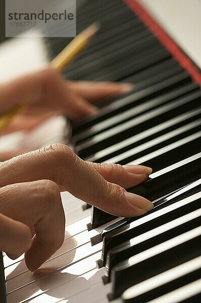 Finger einer Frau mit Bleistift auf den Tasten eines Digitalpianos