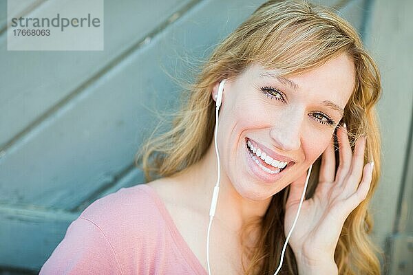 Outdoor portrait of young adult brown eyed woman listening to music with earphones