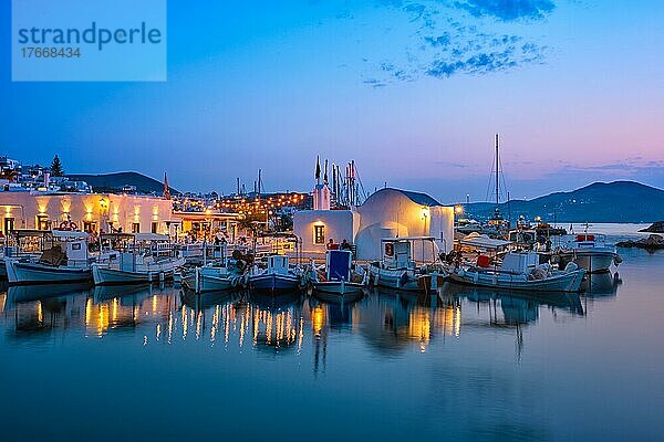 Picturesque view of Naousa town in famous tourist attraction Paros island  Greece with traditional whitewashed houses and moored fishing boats and seaside restaurants and cafe illuminated in night