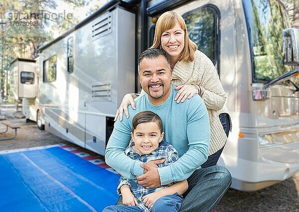 Glückliche junge gemischtrassige Familie vor ihrem schönen Wohnmobil auf dem Campingplatz