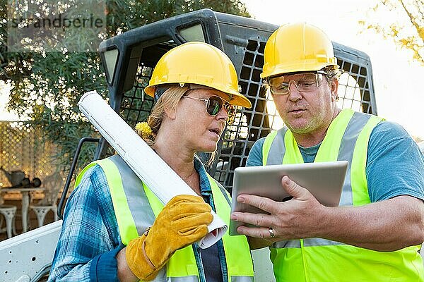 Männliche und weibliche Arbeiter mit technischen Plänen und Computertablett im Gespräch auf der Baustelle
