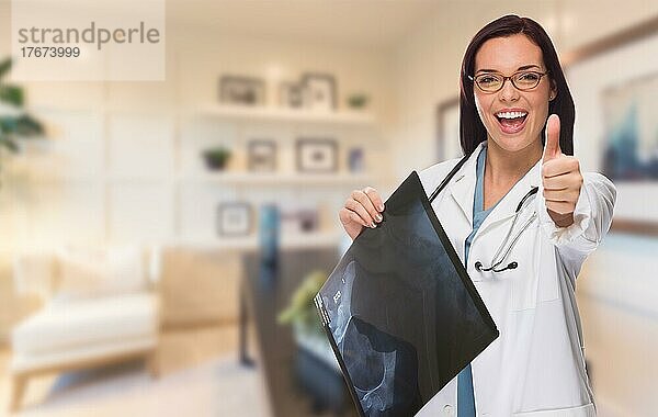 Young female doctor or nurse with thumbs up standing in office holding x-ray