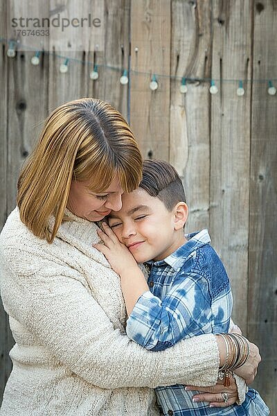 Liebevolle Mutter und gemischtrassiger Sohn umarmen sich am Zaun