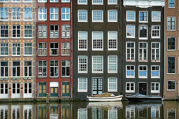 Reihe typischer Häuser und Boot auf dem Amsterdamer Damrak-Kanal mit Spiegelung. Amsterdam  Niederlande  Europa