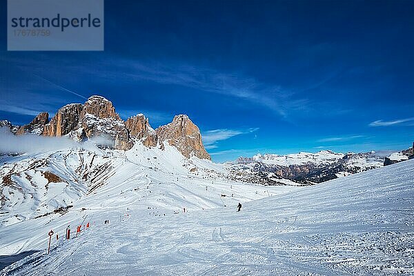 Blick auf eine Piste in einem Skigebiet mit Skifahrern in den Dolomiten in Italien