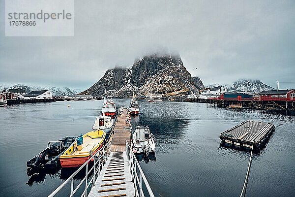 Pier mit Schiffen im Fischerdorf Hamnoy auf den Lofoten  Norwegen  mit roten Rorbu-Häusern. Mit fallendem Schnee  Europa