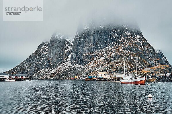 Ein Fischerboot im Fischerdorf Hamnoy auf den Lofoten  Norwegen  mit roten Rorbu-Häusern. Mit fallendem Schnee  Europa