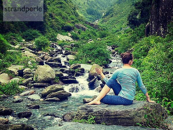Yoga-Übung im Freien  Frau macht Ardha matsyendrasanaasana asana  halbe Wirbelsäule Twist Pose an tropischen Wasserfall im Himalaya in Indien. Vintage Retro-Effekt gefiltert Hipster-Stil Bild