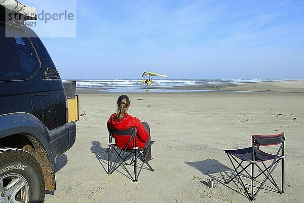 Frau sitzt auf Campingstuhl neben Geländefahrzeug am Strand und beobachtet ein startendes Leichtflugzeug  ULM  Torres  Rio Grande do Sul  Brasilien  Südamerika