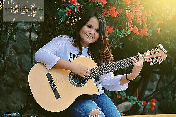 Ein Mädchen sitzt und spielt Gitarre im Freien  Porträt eines lächelnden Mädchens beim Gitarrenspiel  Lebensstil eines Mädchens beim Gitarrenspiel im Freien