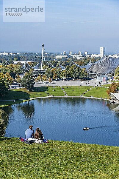 Zwei Personen sitzen im Park mit Olympiasee  Olympiapark München  Bayern  Deutschland  Europa