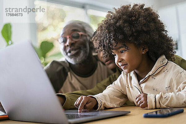 Smiling grandparents with granddaughter using laptop