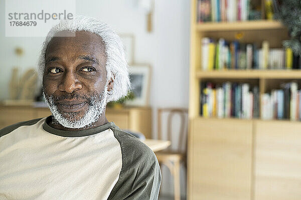 Lächelnder älterer Mann sitzt im Wohnzimmer