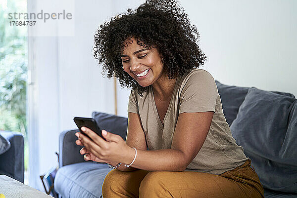 Frau benutzt Smartphone  während sie im Wohnzimmer sitzt