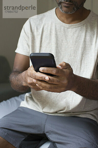Mann benutzt Smartphone  während er im Schlafzimmer sitzt